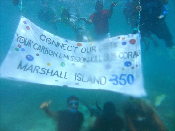 Activists hold a banner in front of a damaged coral reef in the vulnerable Marshall islands. Rising temperatures and increased CO2 uptake are raising the acidity of the ocean, which bleaches and ultimately may kill fragile coral reefs. Photo courtesy of: 350.org.