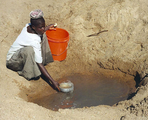 Access to clean water is most difficult in Africa. Here a woman in Tanzania gathers water from a hole in a riverbed. Photo by: Bob Metcalf.